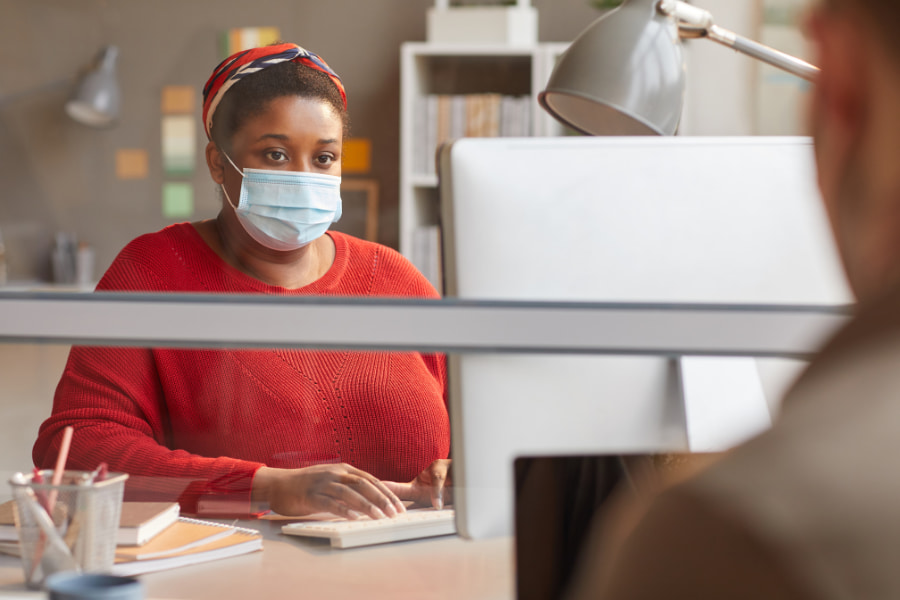 Person working in an office with a mask on at a computer
