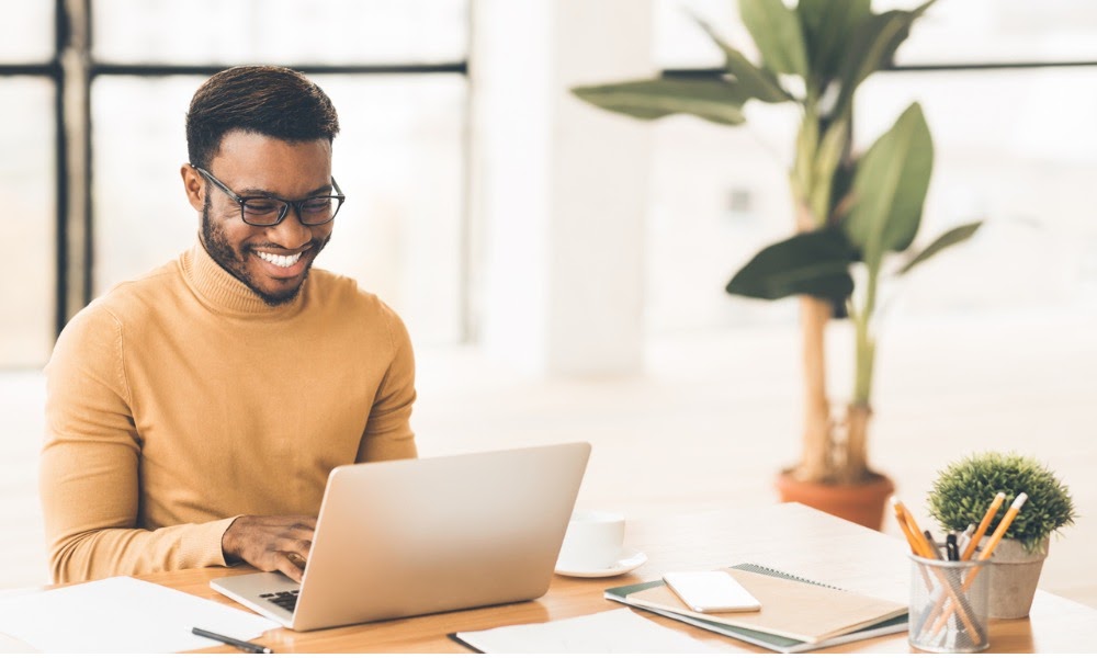 A young employee smiles while working on a laptop to access digital HR tools.